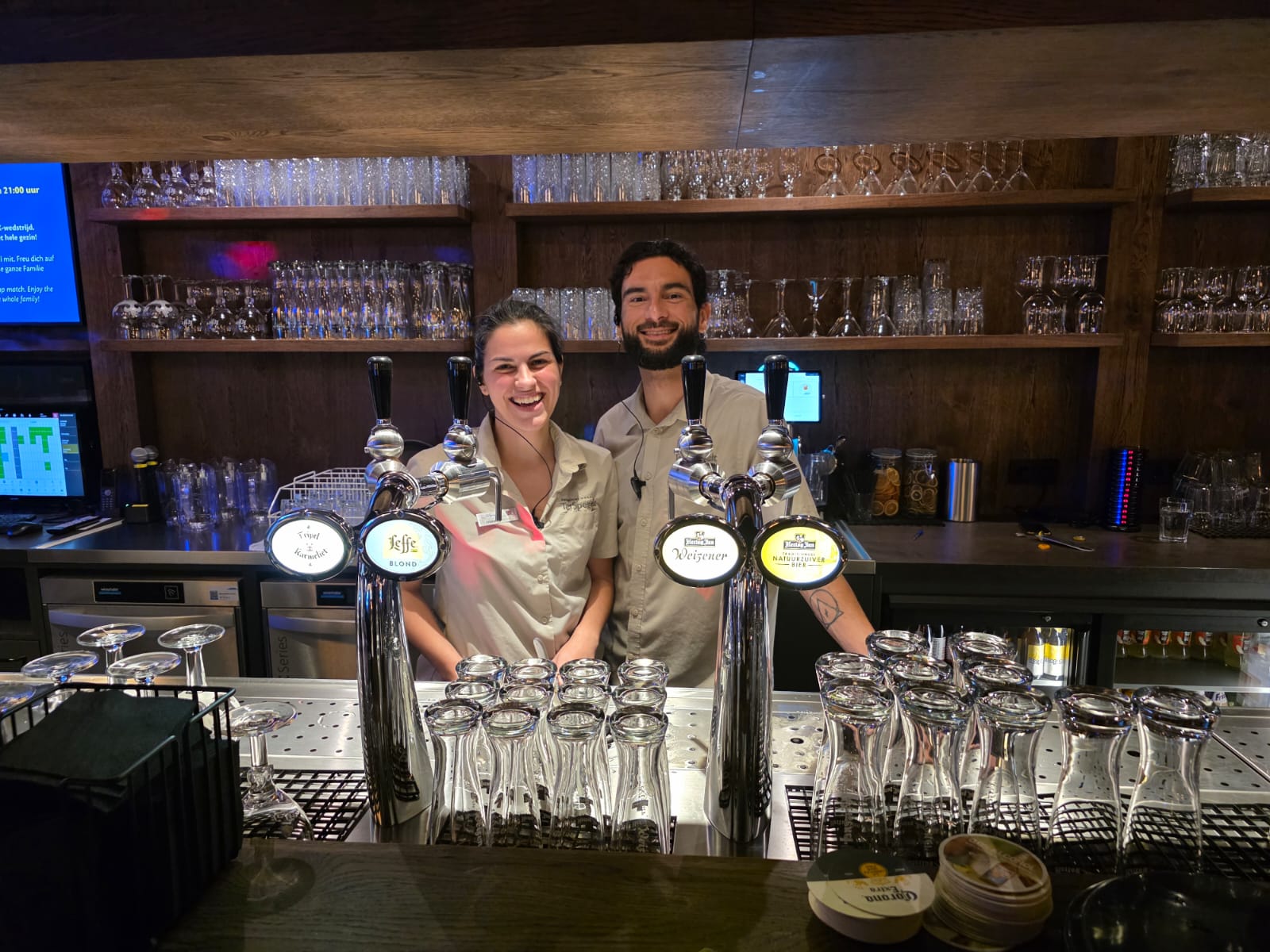 Diana en João samen achter de bar van de bowlingpub, allebei lachend
