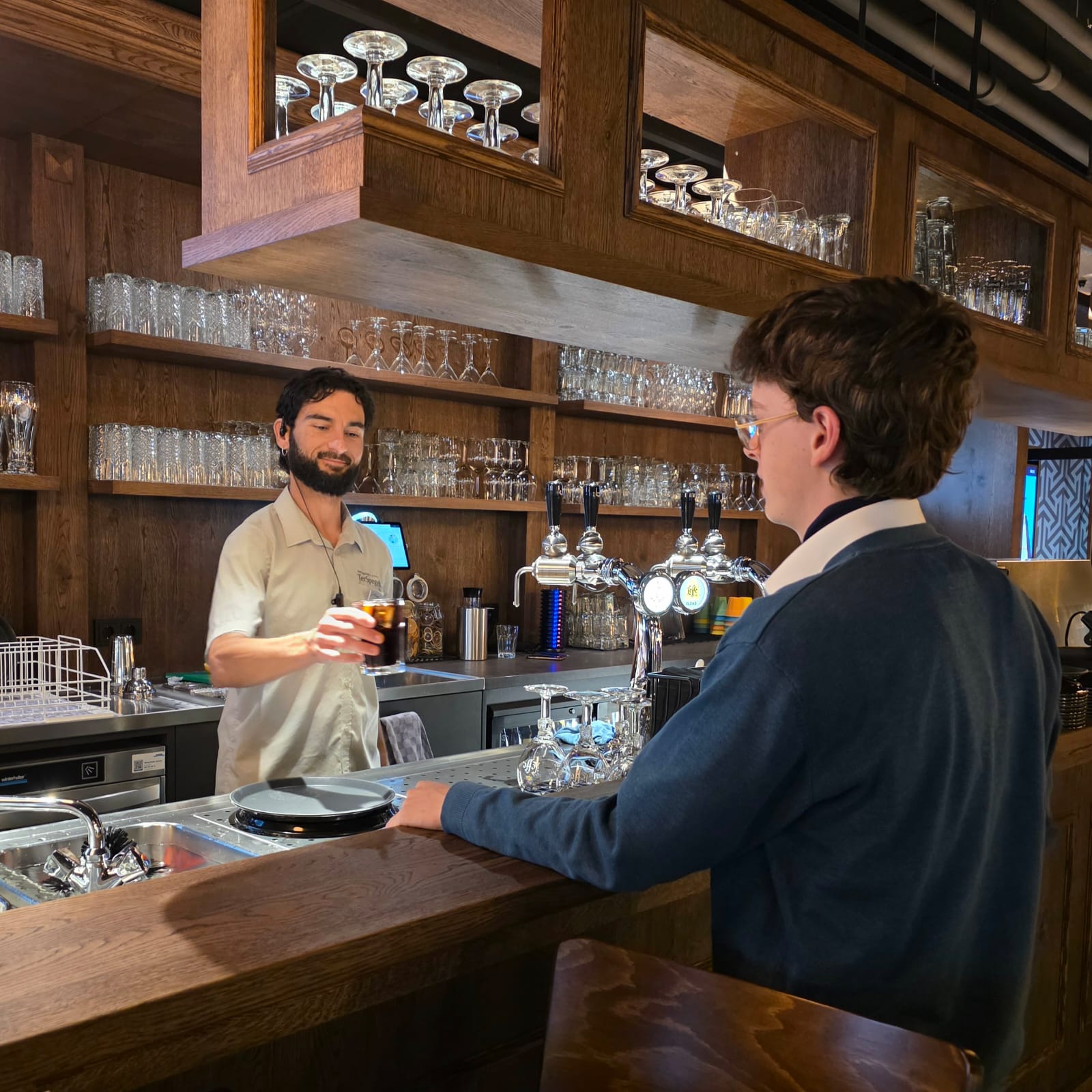 João geeft een gast een drankje aan de bar van de bowlingpub