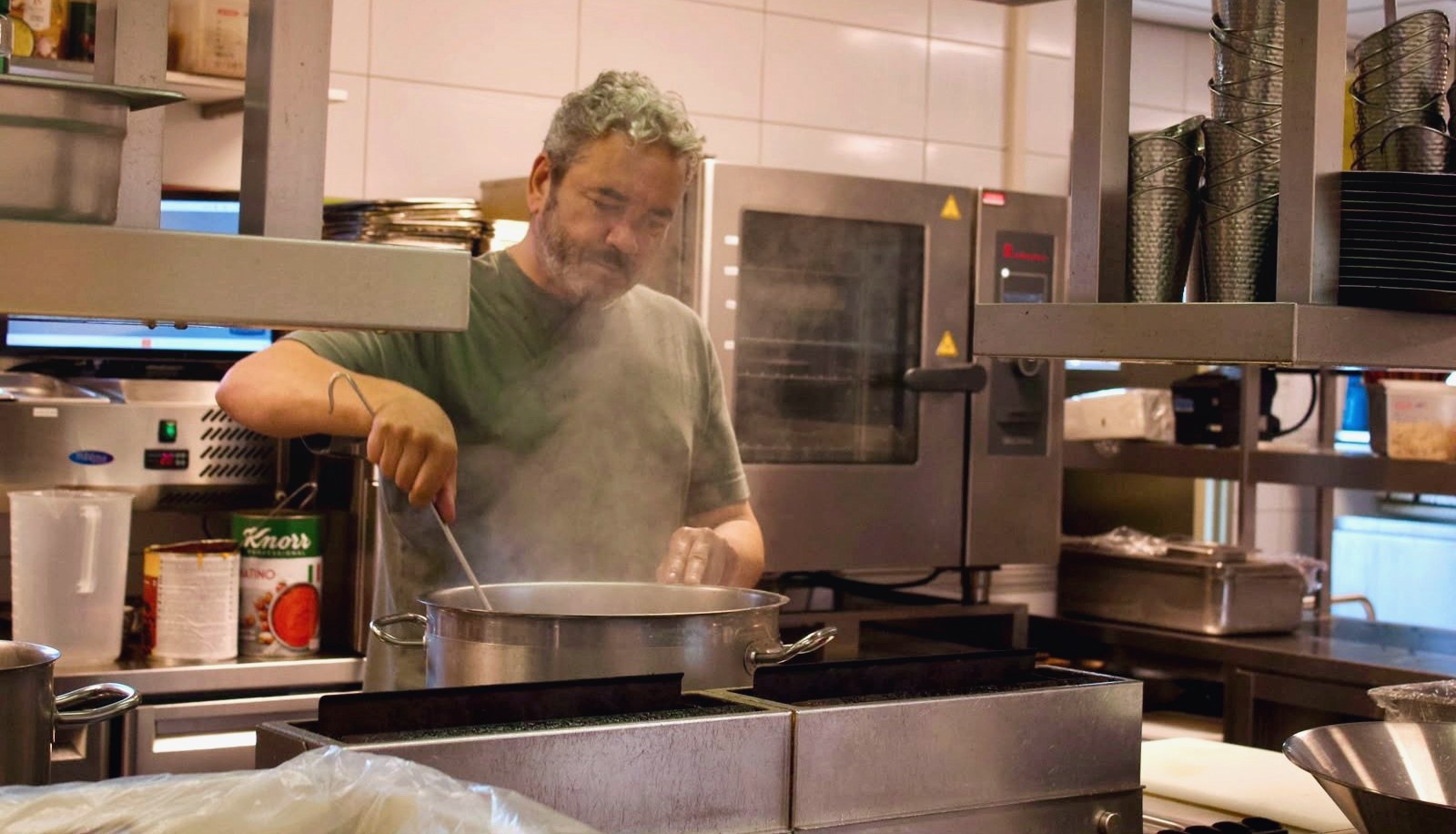 Keukenmedewerker roert in een grote soeppan in de keuken van een horecabedrijf