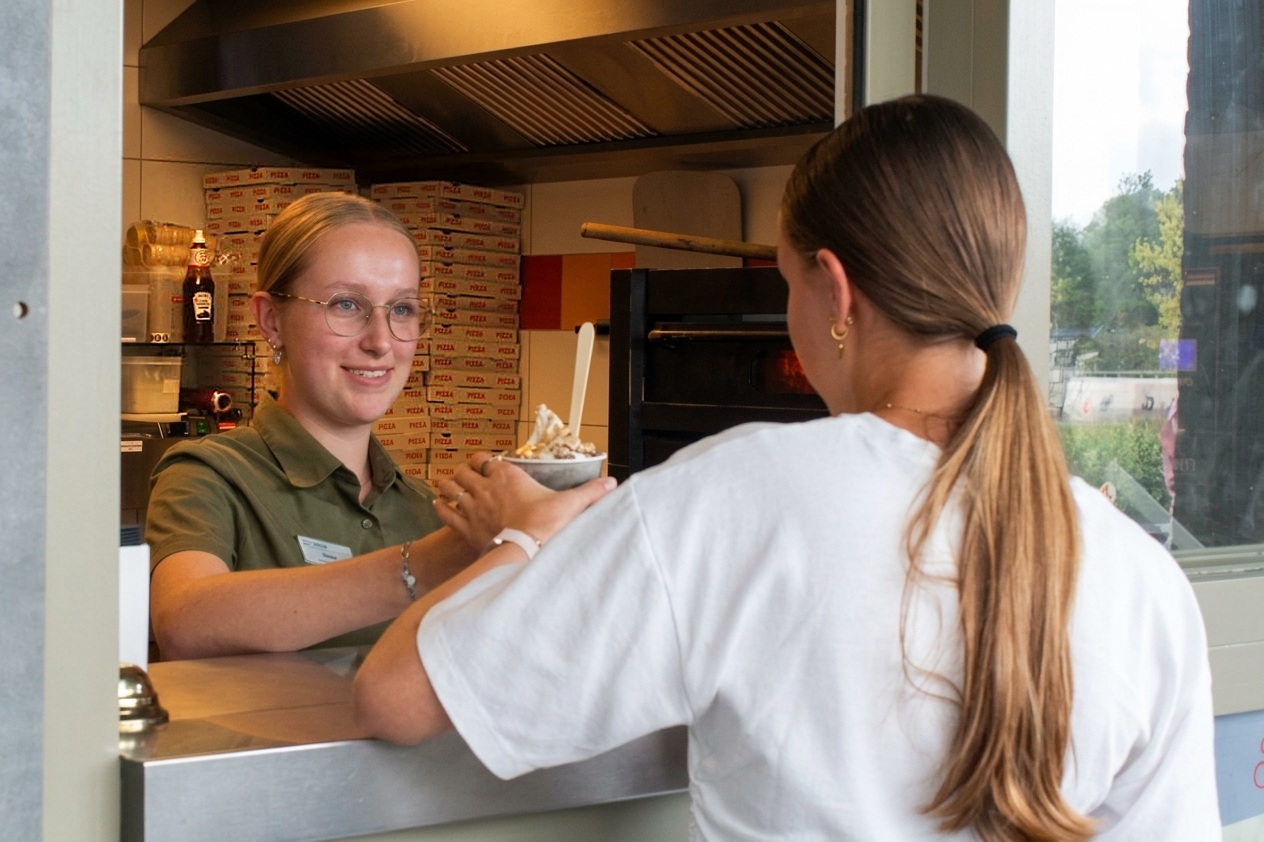 Medewerker geeft een gast met een glimlach een ijsje aan bij de snackbar van het recreatiepark